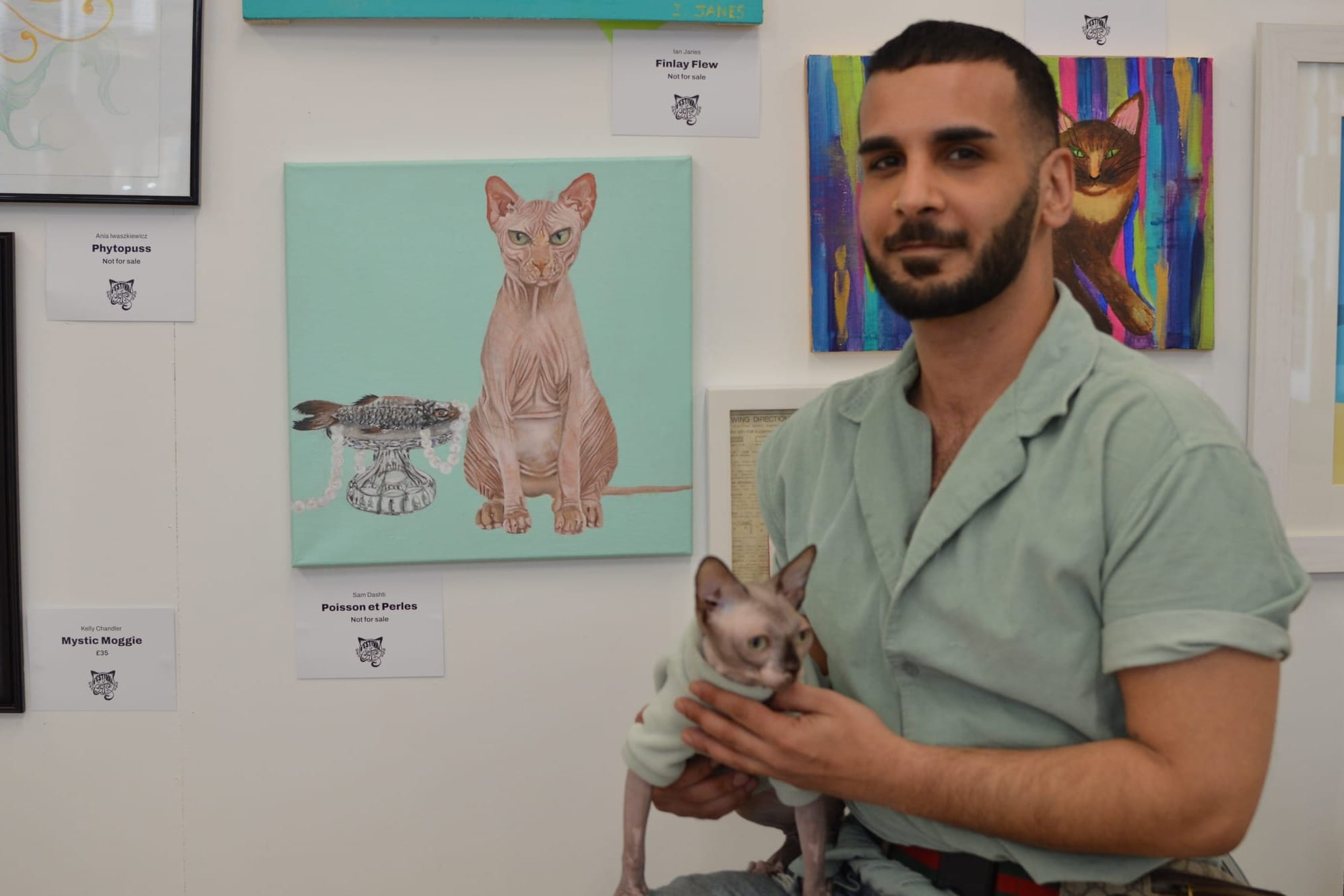 Man poses with a hairless cat in front of a picture of a hairless cat