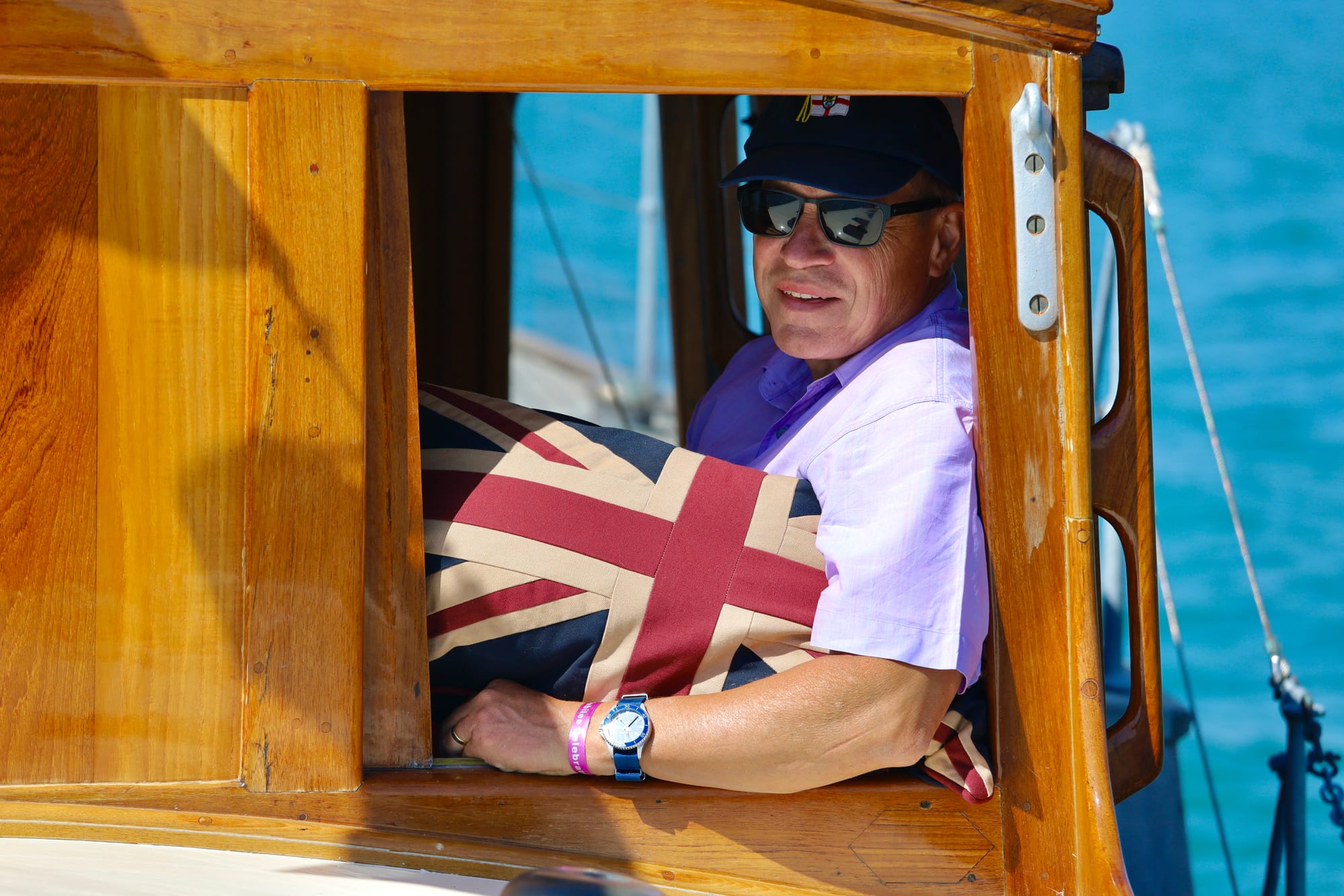 Man in a cabin window of a vintage boat holding a Union Jack cushion