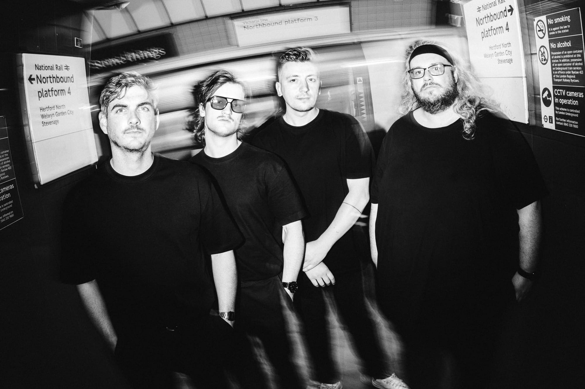 Four men dressed in black posing on a subway platform.