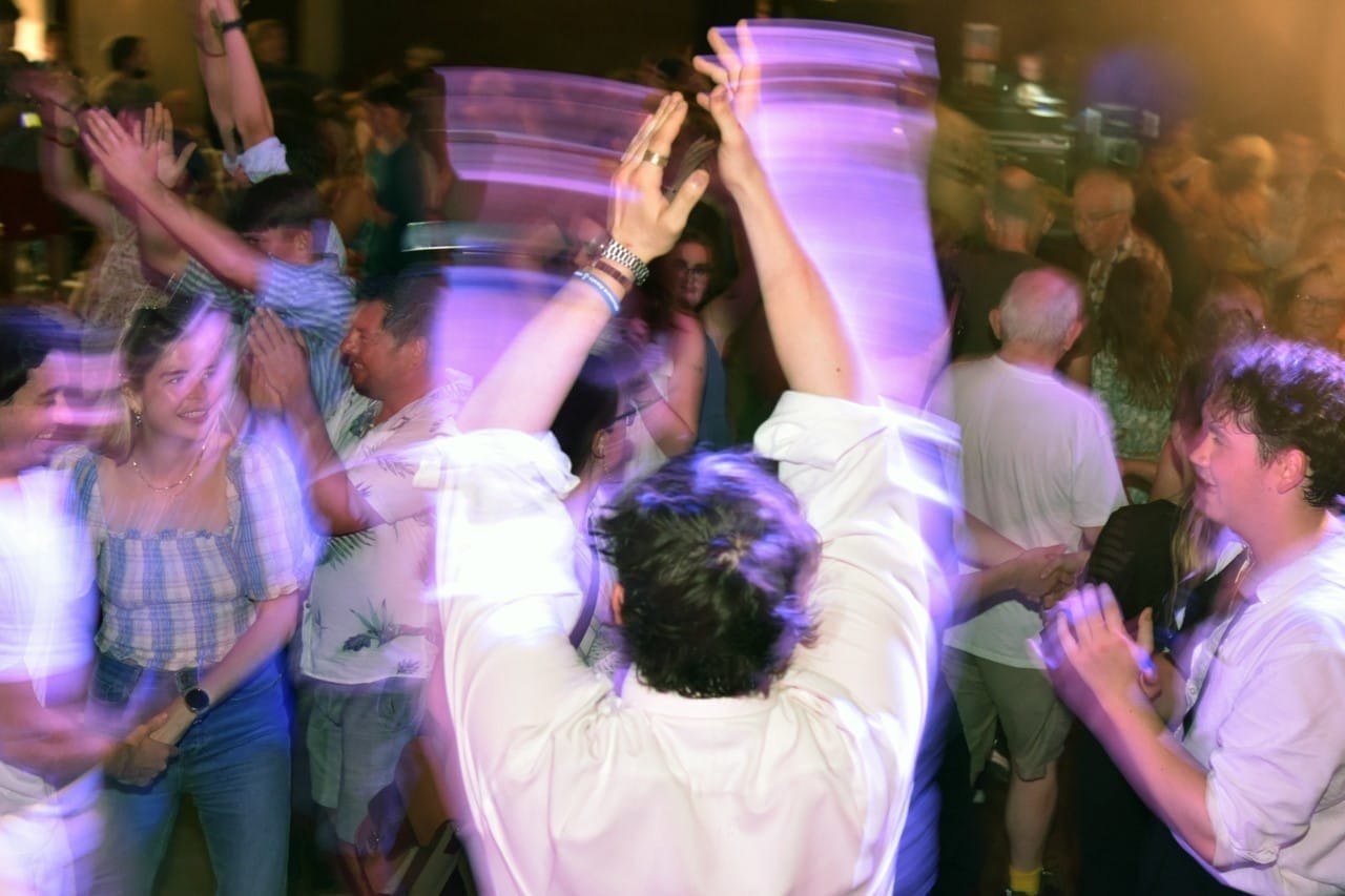 In a crowd a man in a white shirt claps his hands while dancing.