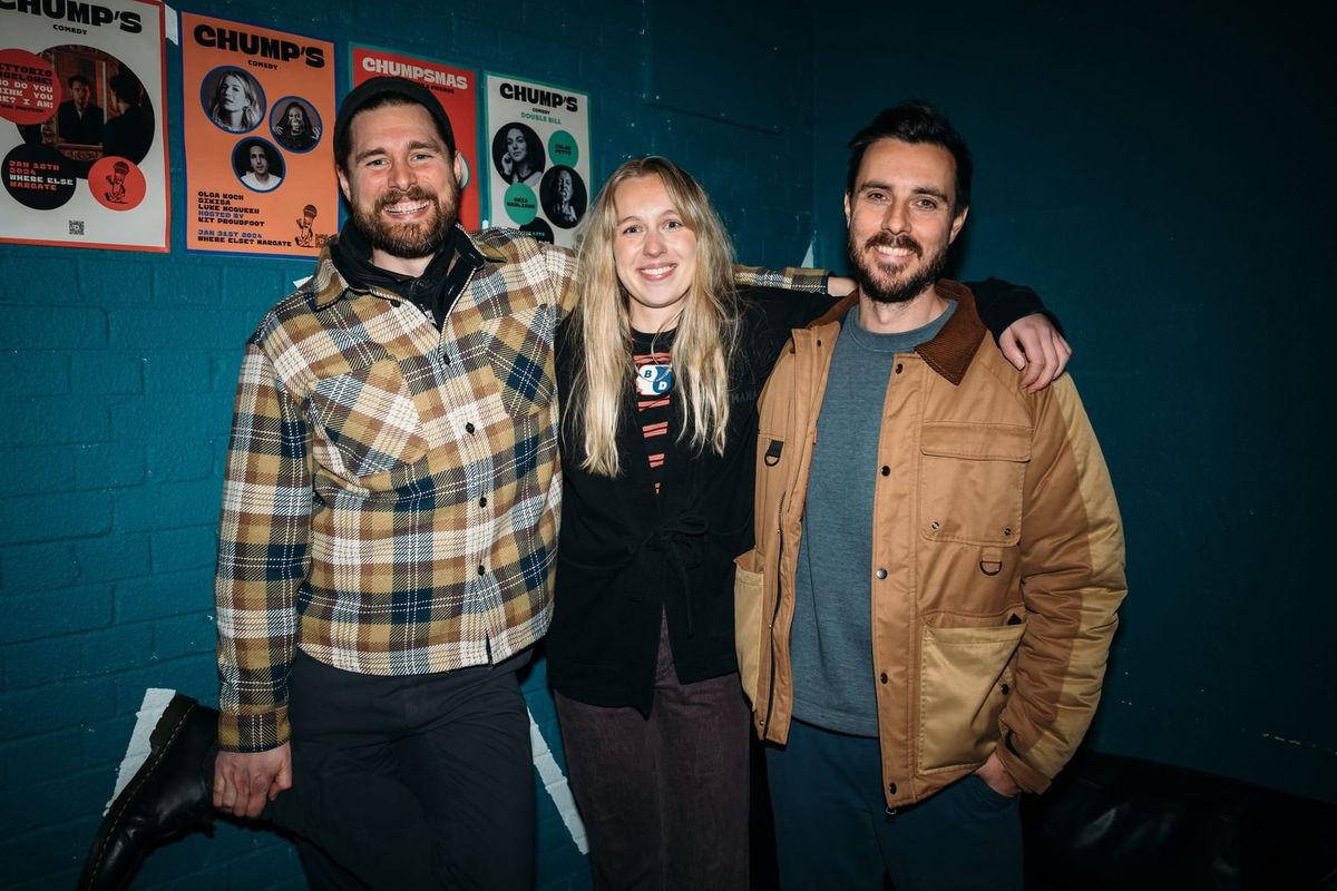 Two men and a woman stand against a blue wall