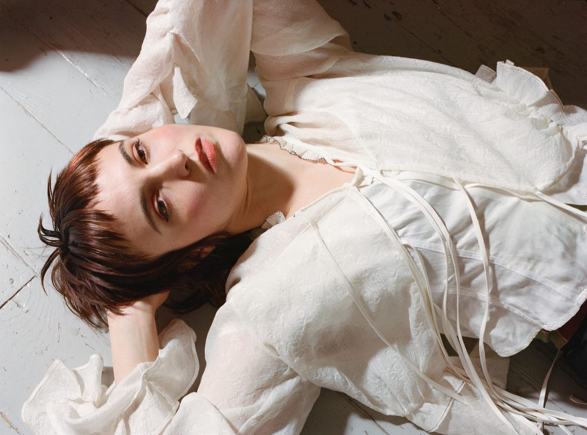 A woman with short hair wearing a white shirt reclines on the ground