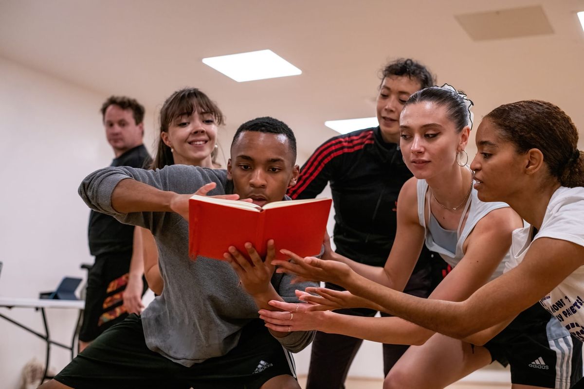 A group of young dancers gather around a red book