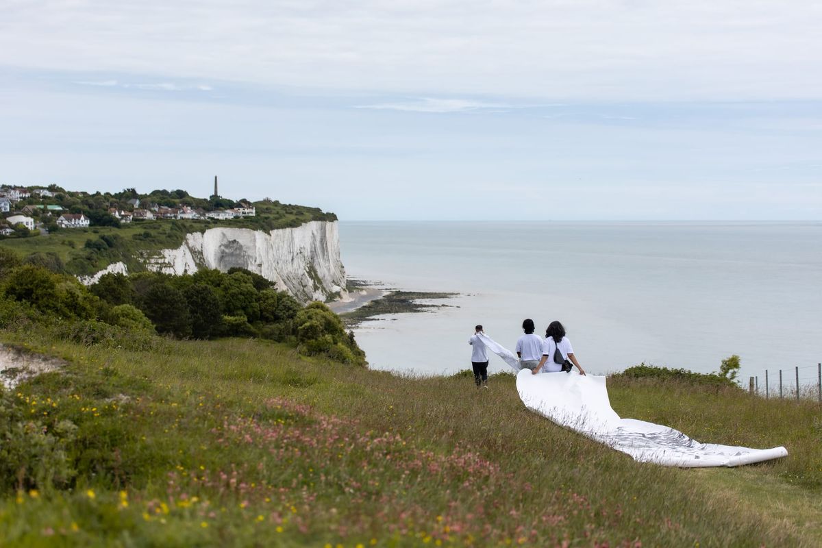 Three people carry a strip of white material across a clifftop