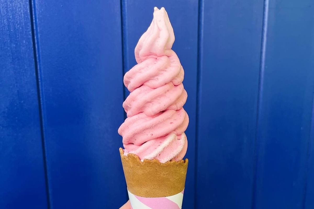 A tall, pink ice cream in a cone against a black background. 
