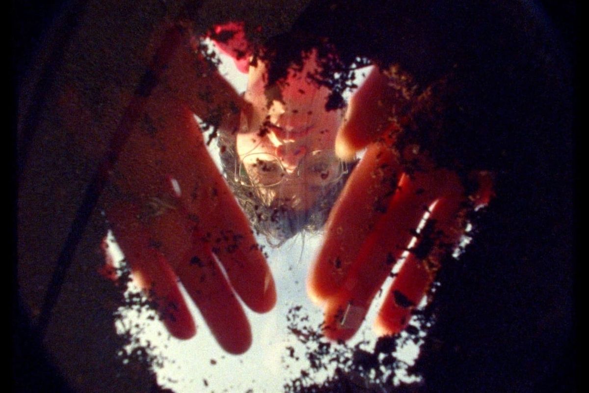 A woman wearing glasses looks down through earth cleared away with her hands