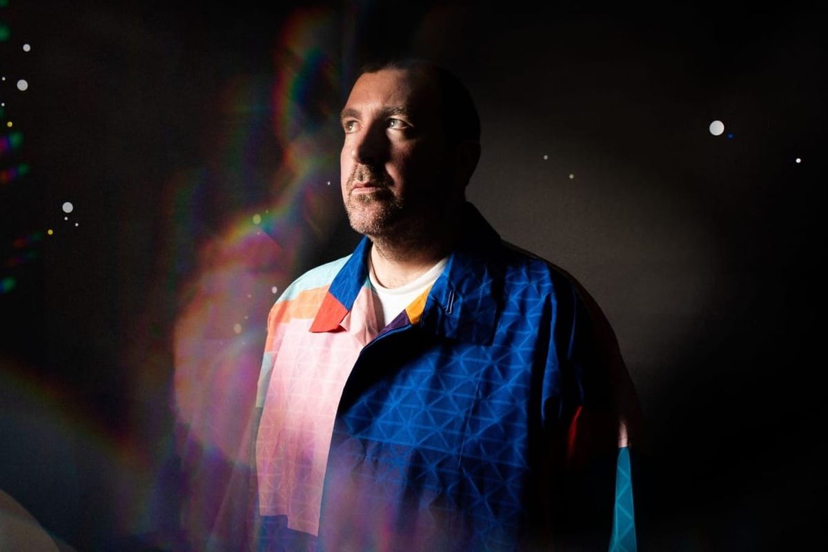 A man stands in a colourful, predominantly blue shit looking off to the side of the frame.