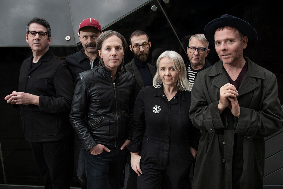 Seven people dressed in black. One wears a red hat. 