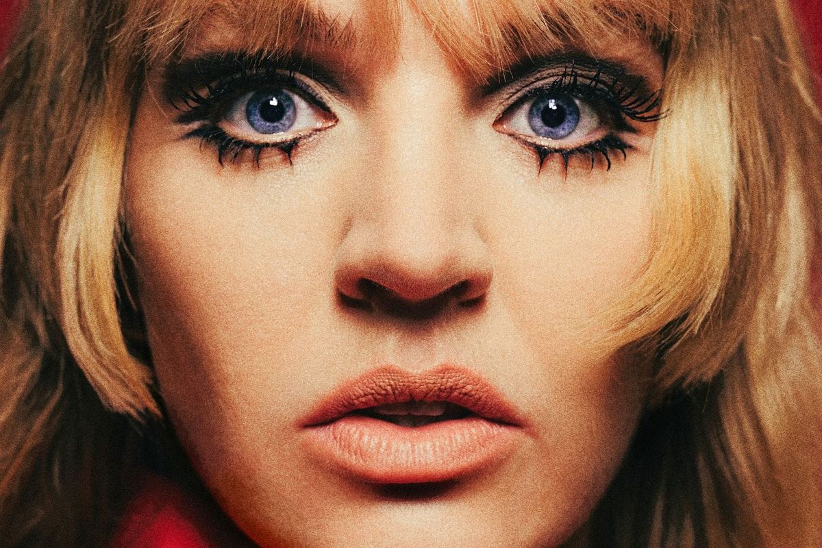 A blonde woman with blue eyes stares into the camera