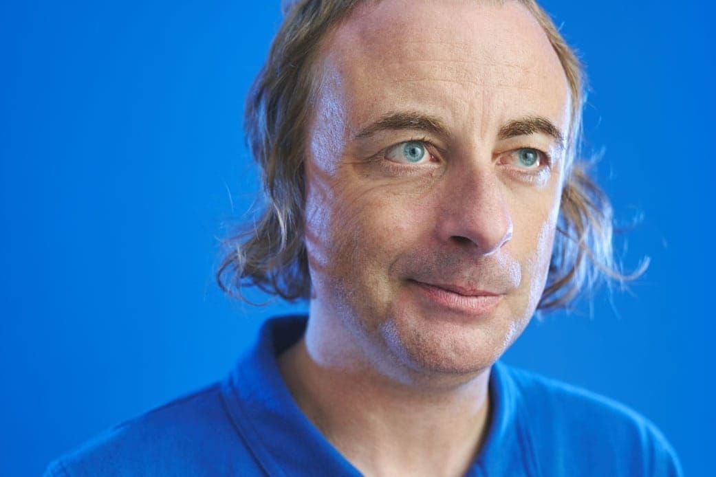 A Man in a blue shirt against a blue background looks off to the side
