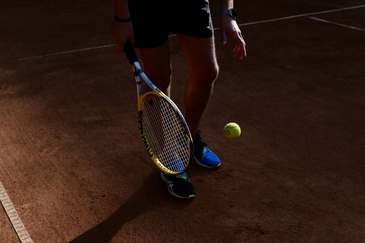 A person wearing blue trainers holding a tennis racquet on a tennis court. 