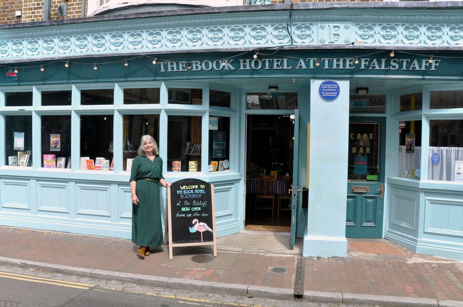 A woman in a green dress stands outside a hotel