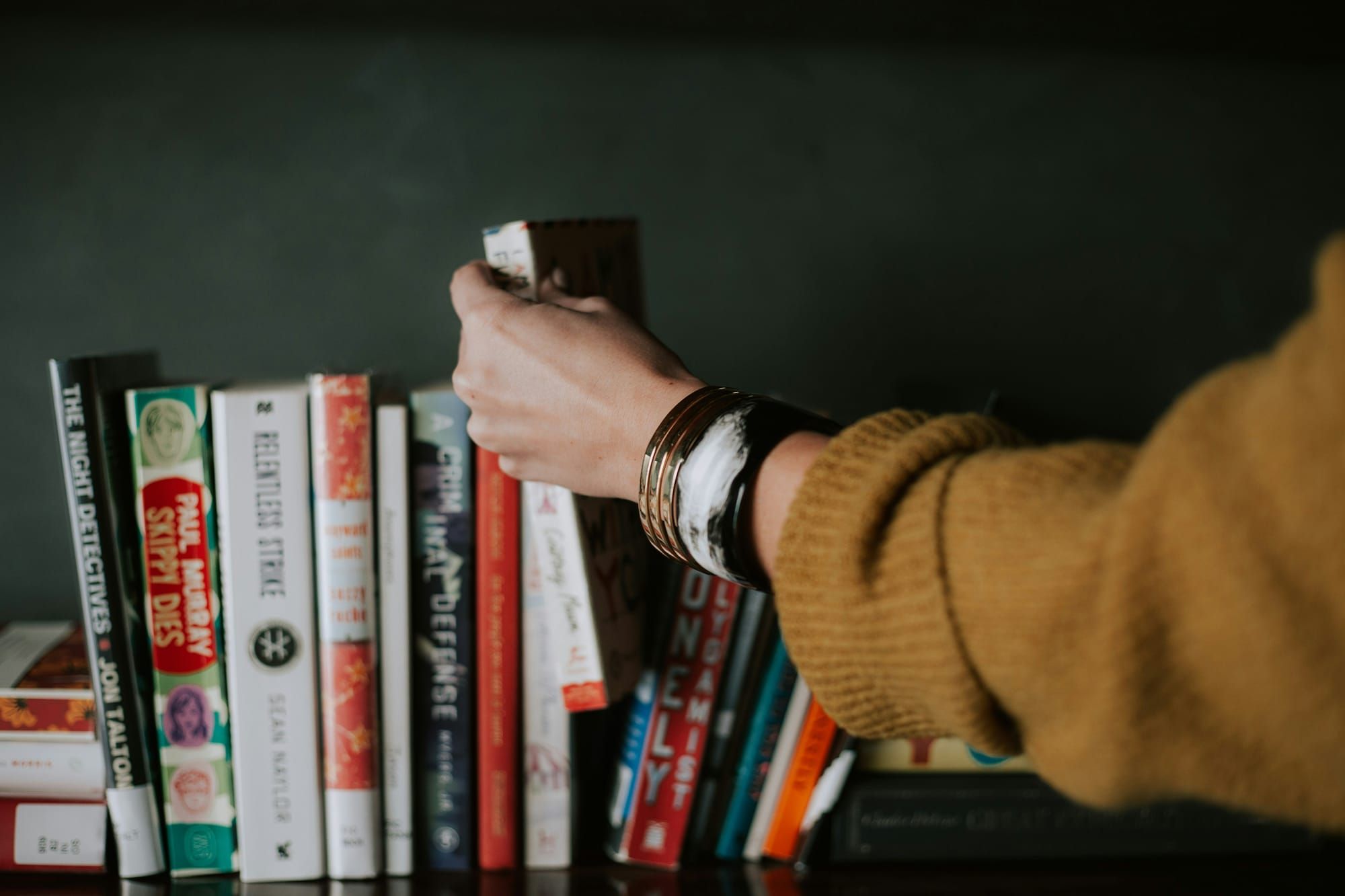 A woman's hand reaching for a book in a pile of them.