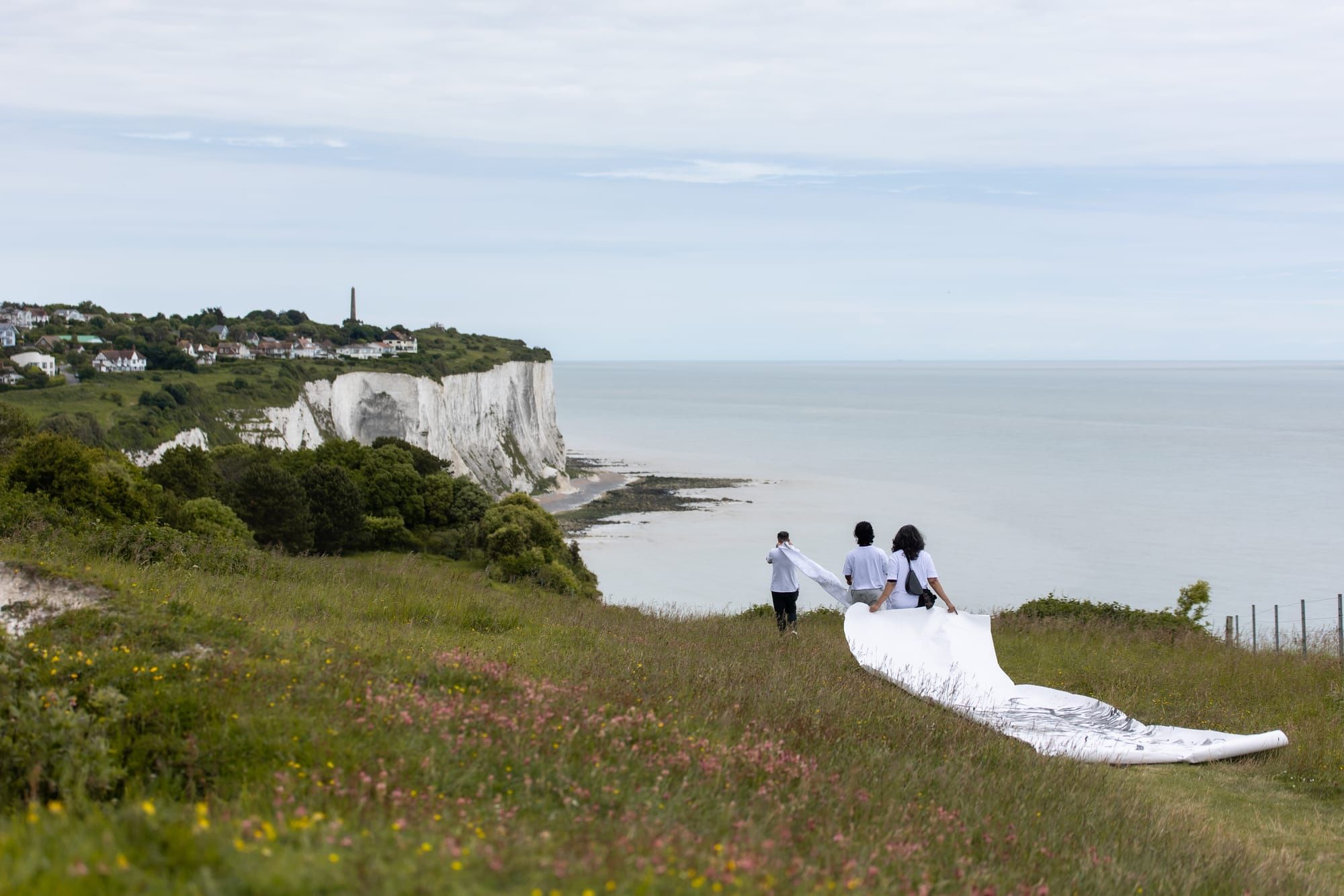 Three people carry a strip of white material across a clifftop