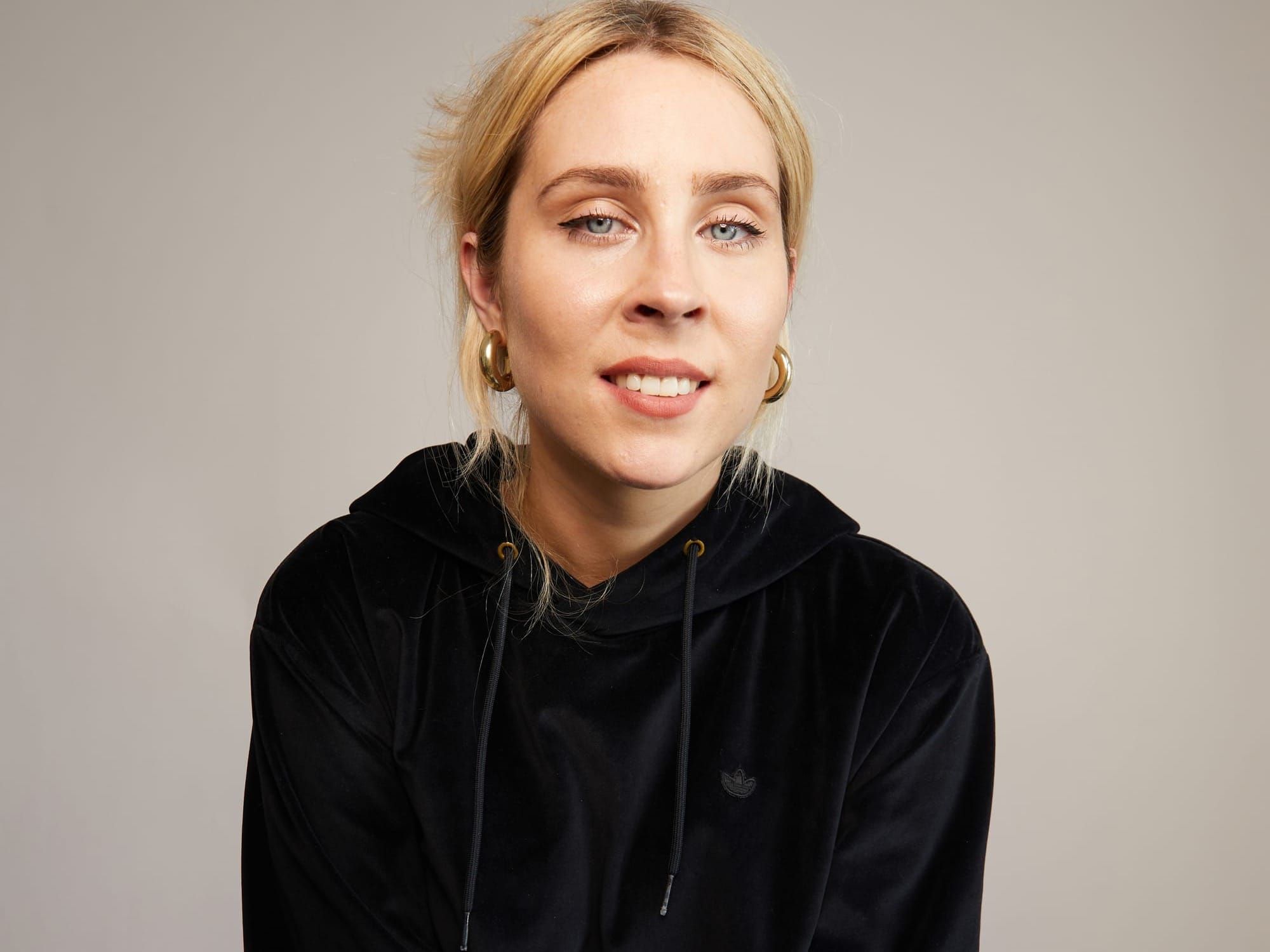 A blonde woman wearing a black hoodie stares into the camera