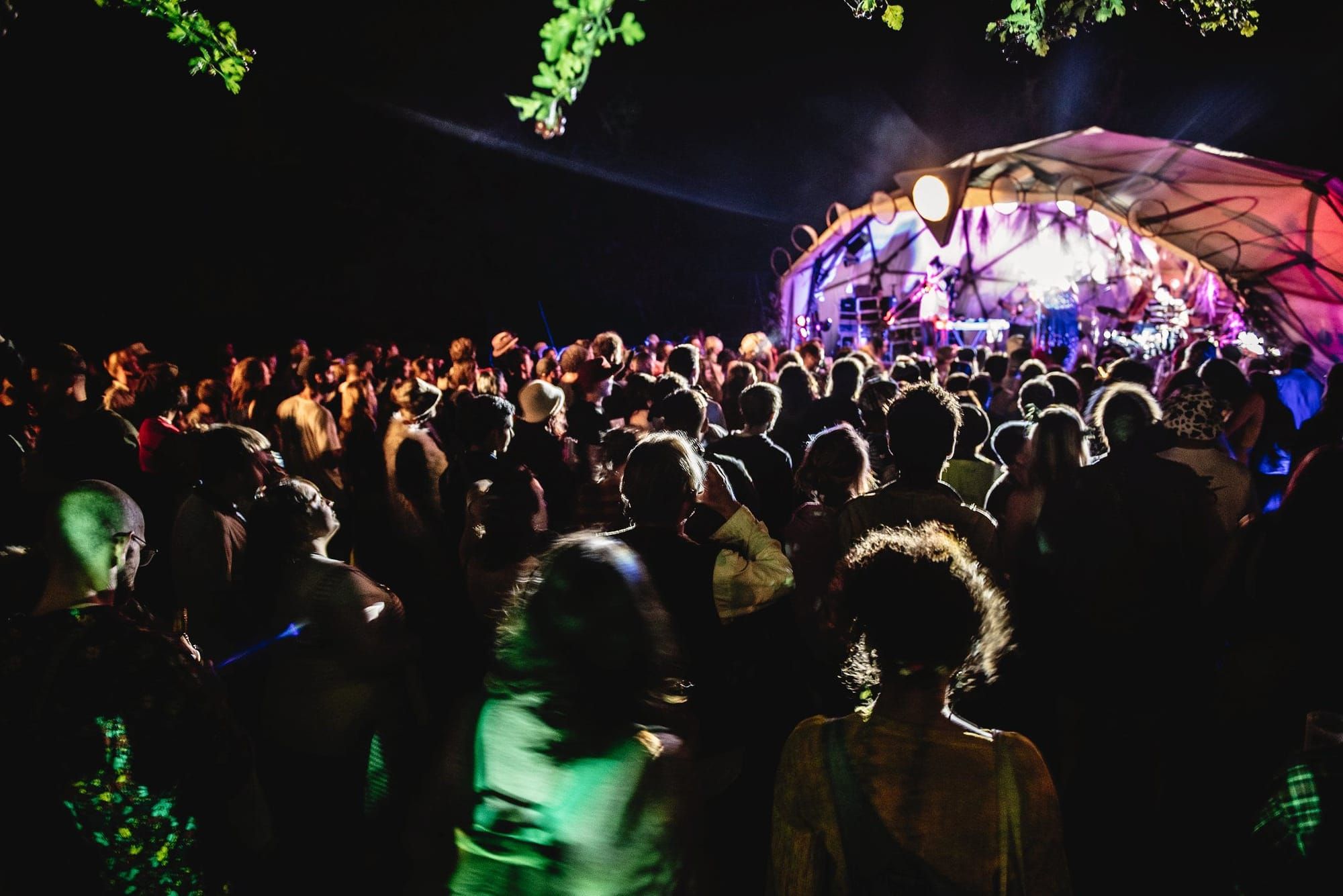 A large crowd of people at a festival at night watching a performer on stage. 