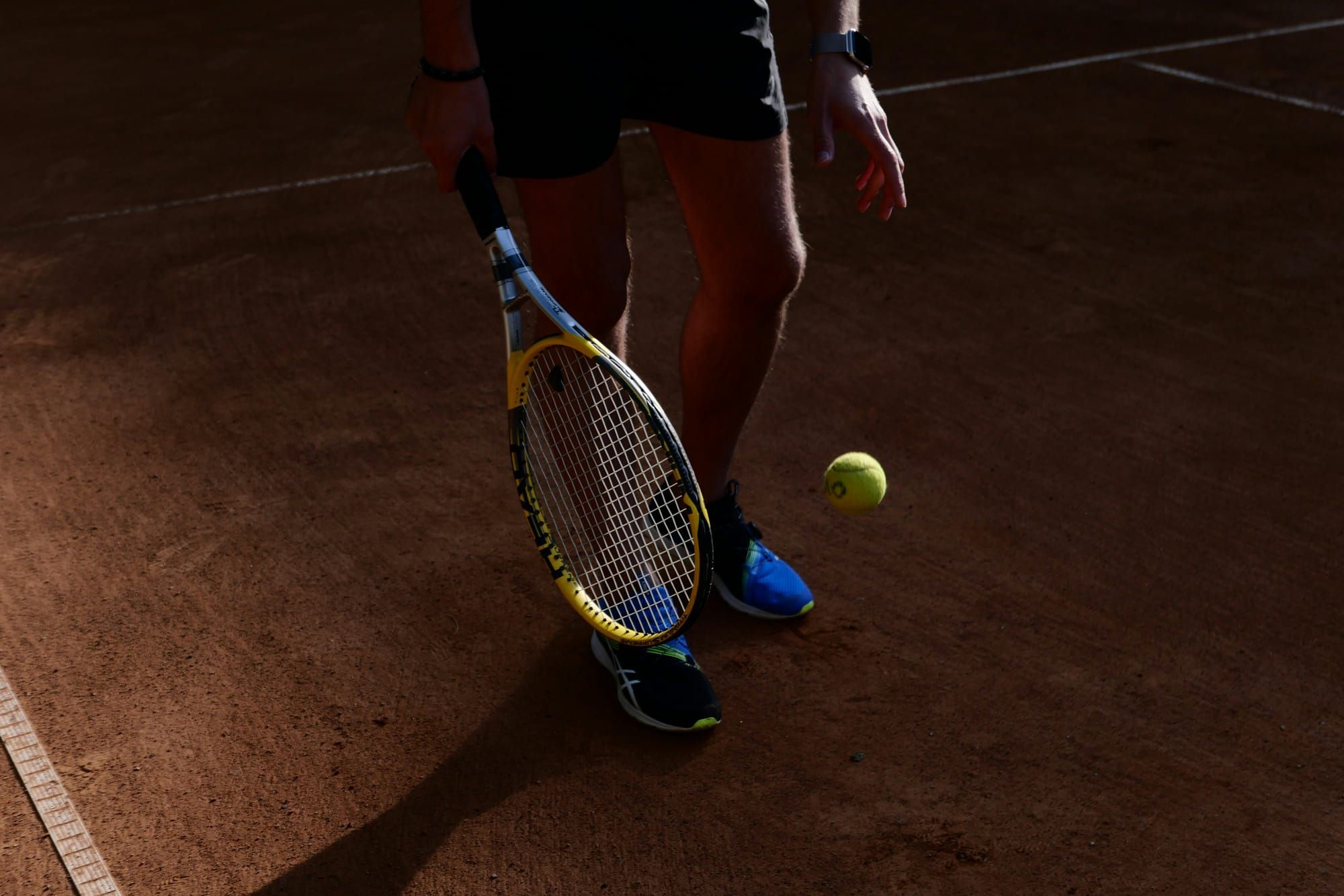 A person wearing blue trainers holding a tennis racquet on a tennis court. 