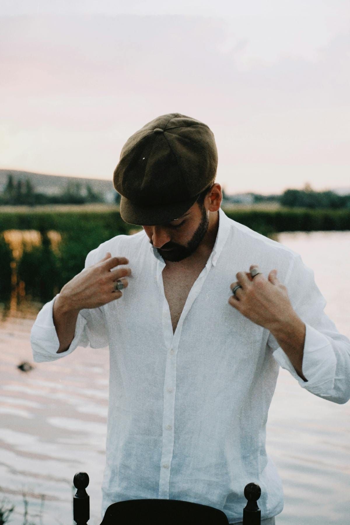 Man in white linen shirt and newsboy cap by a lake at sunset, the breezy mild look for 72 degree weather