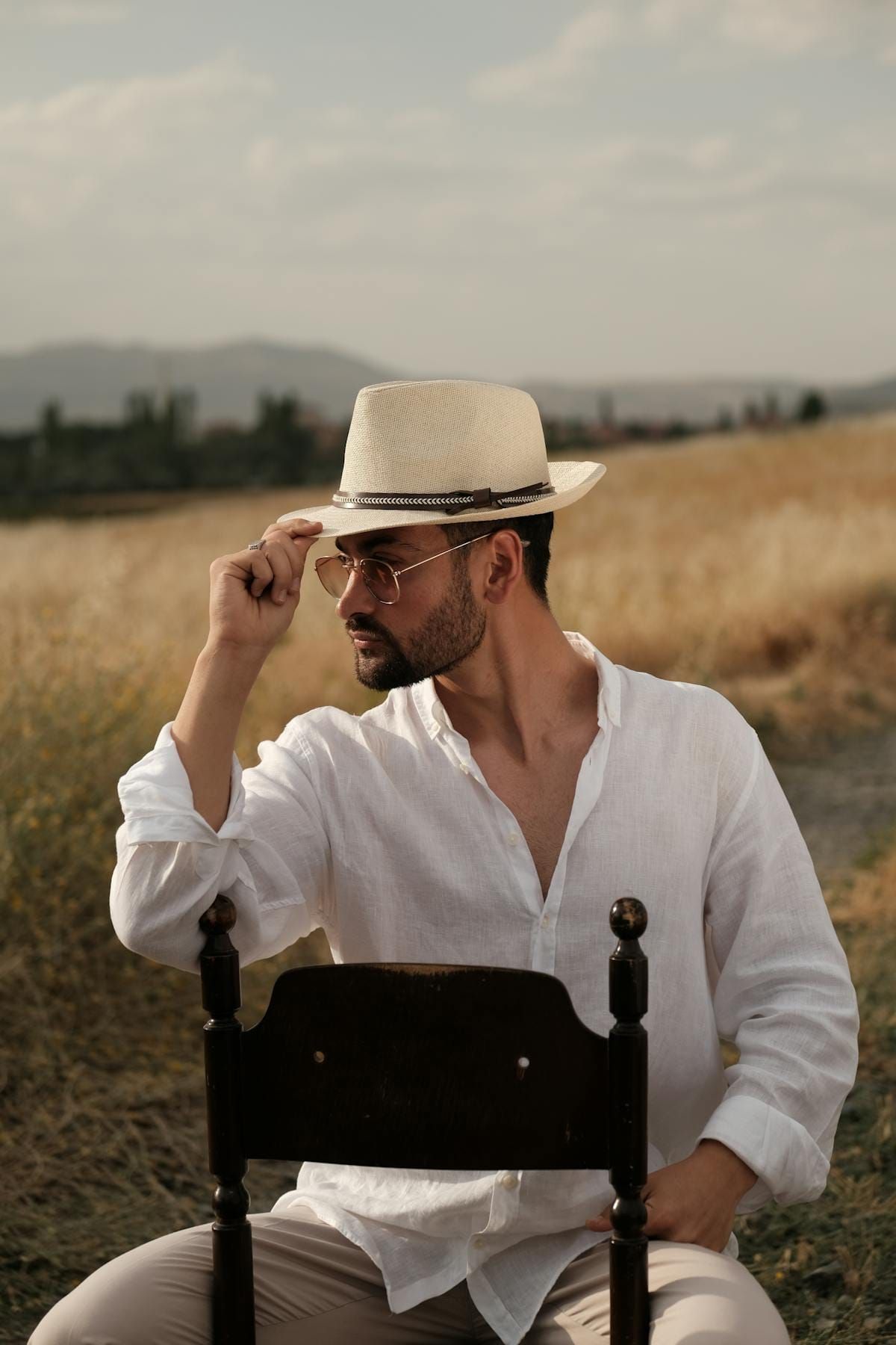 Man in white linen shirt and straw hat sitting in a sunny rural field, the breathable warm look for 78 degree weather