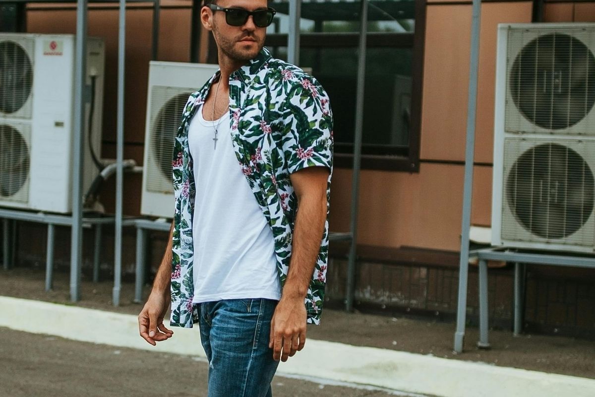 Man in a casual short-sleeve shirt and sunglasses walking confidently down an urban street on a hot summer day