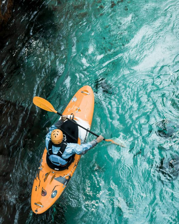 Kayaker in an orange kayak paddling through clear turquoise water