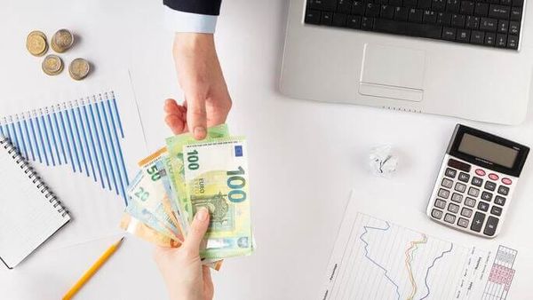 o femeie înmână euro unui bărbat, pe masă stau câteva coins, calculator, laptop