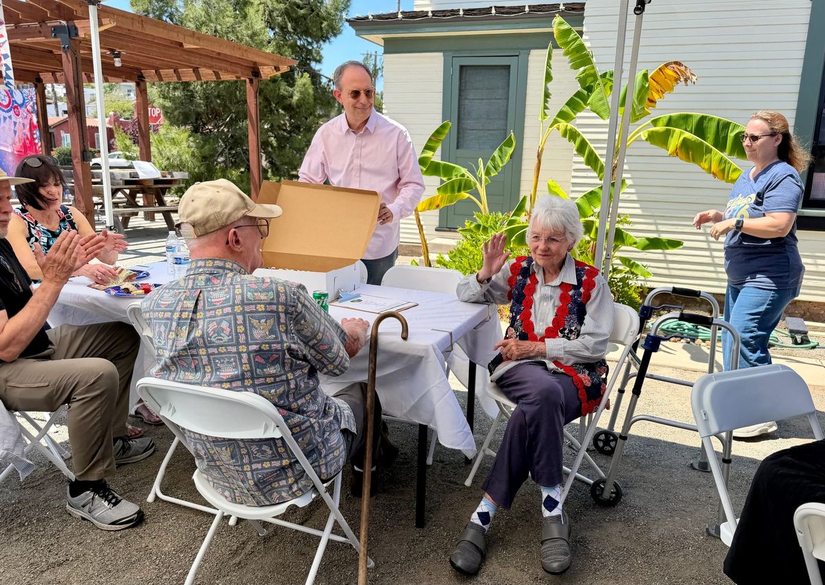 People sat and stood around an outdoor table celebrating 