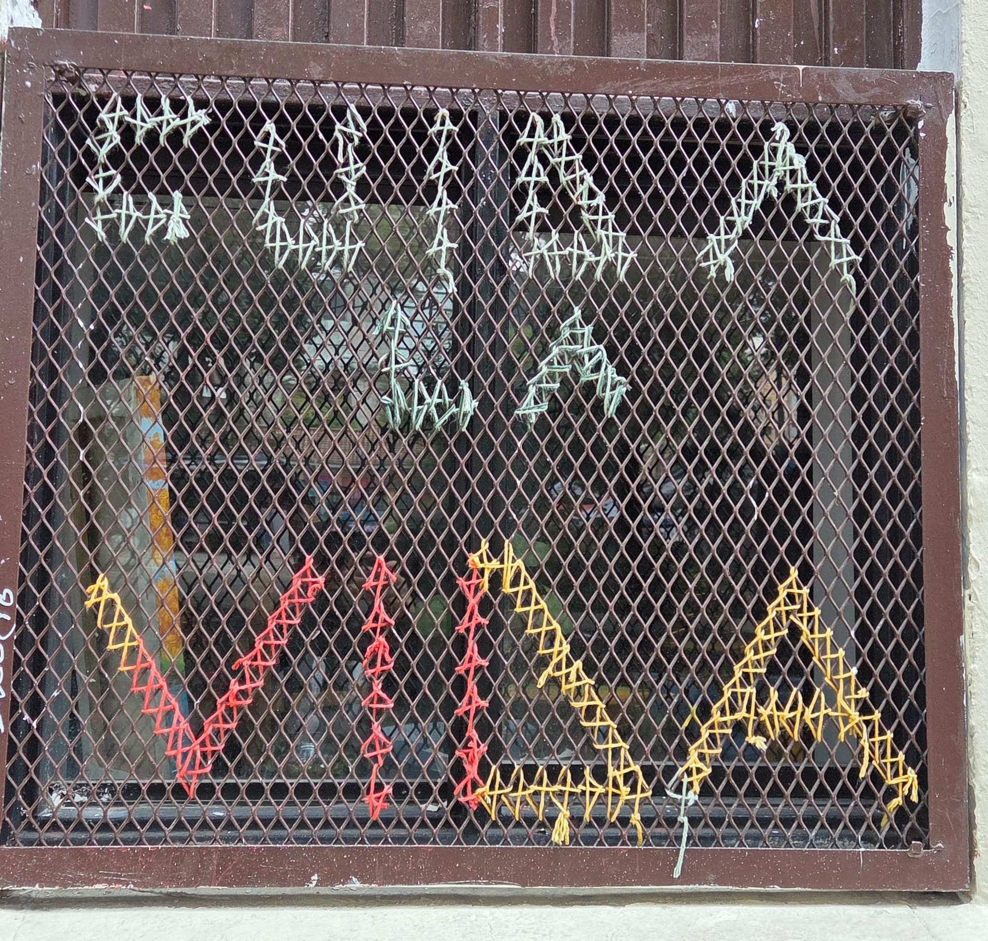 Fotografia de una rejilla en una ventana con el texto: "cuida la vida".