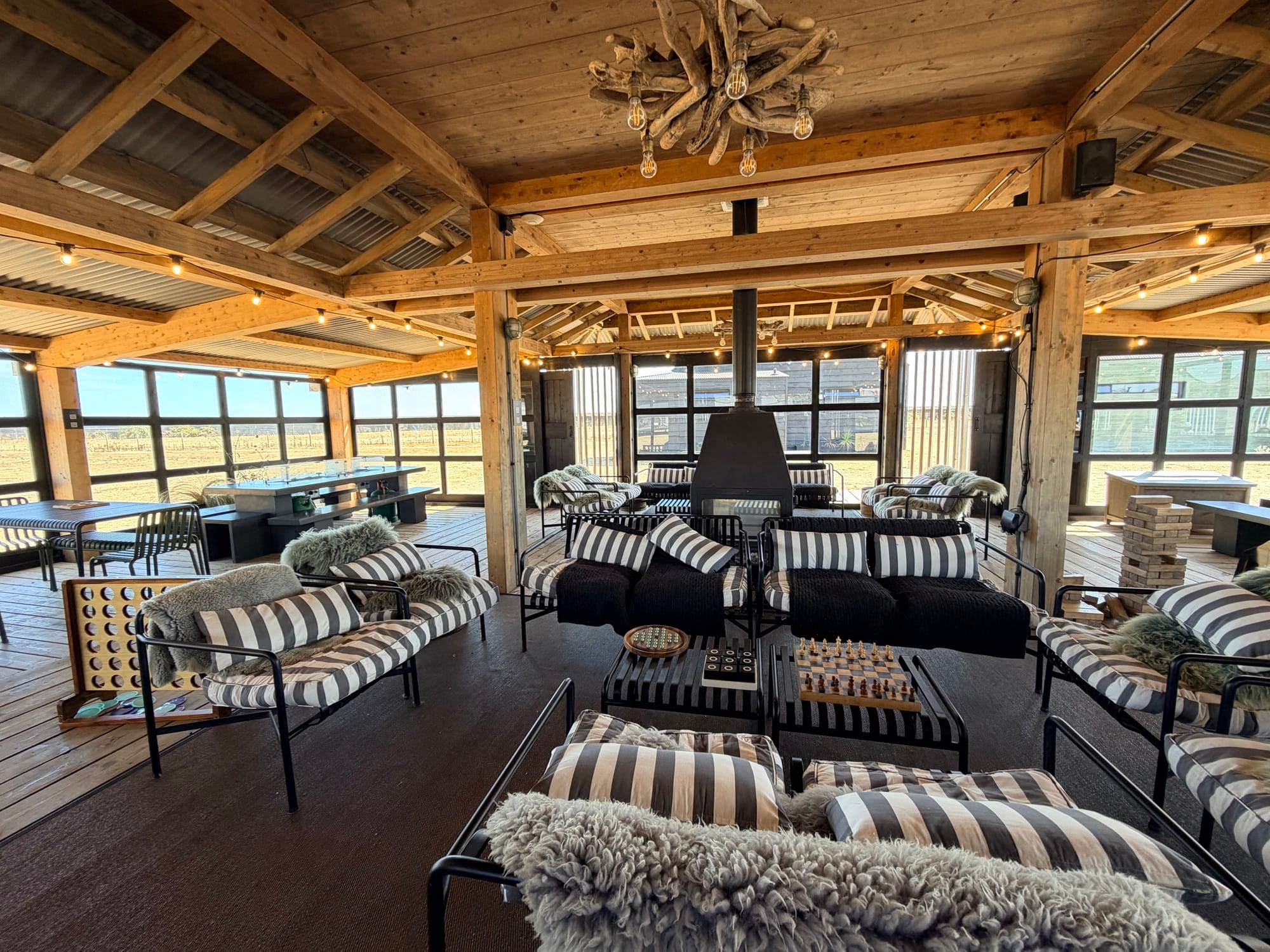 Communal lounge barn at Cabu by the Sea with central log burner, cushioned sofas, sheepskin throws and board games