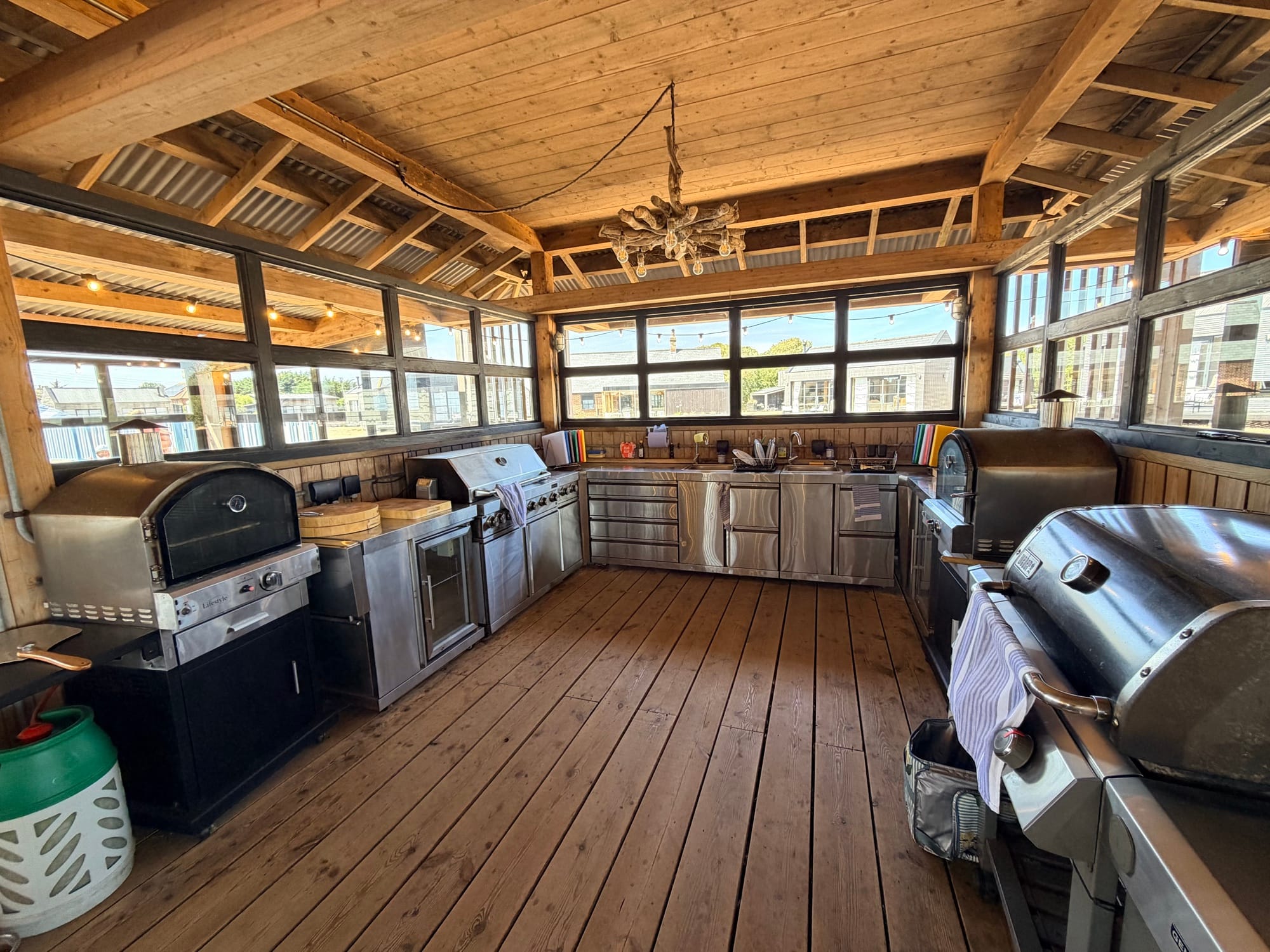 Timber-framed communal outdoor kitchen at Cabu by the Sea with gas pizza oven, stainless barbecues and festoon lights