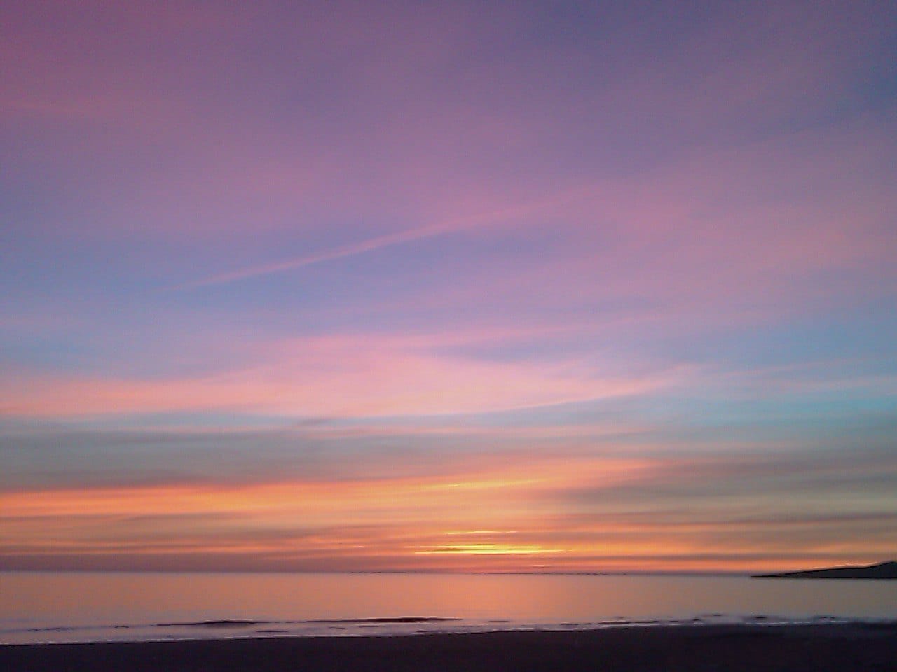 Dawn over the sea at Cala Millor, pink and orange sky above a still bay