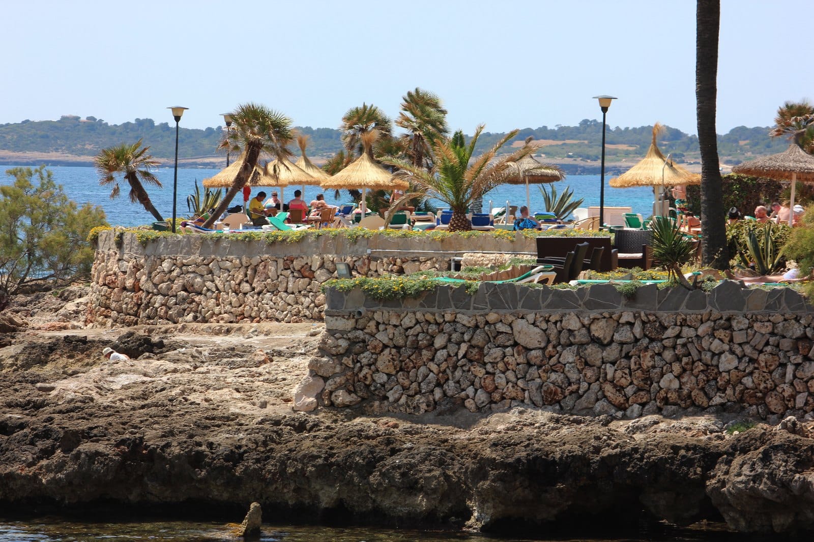 Terrace café with straw parasols above the rocks on the Cala Millor seafront
