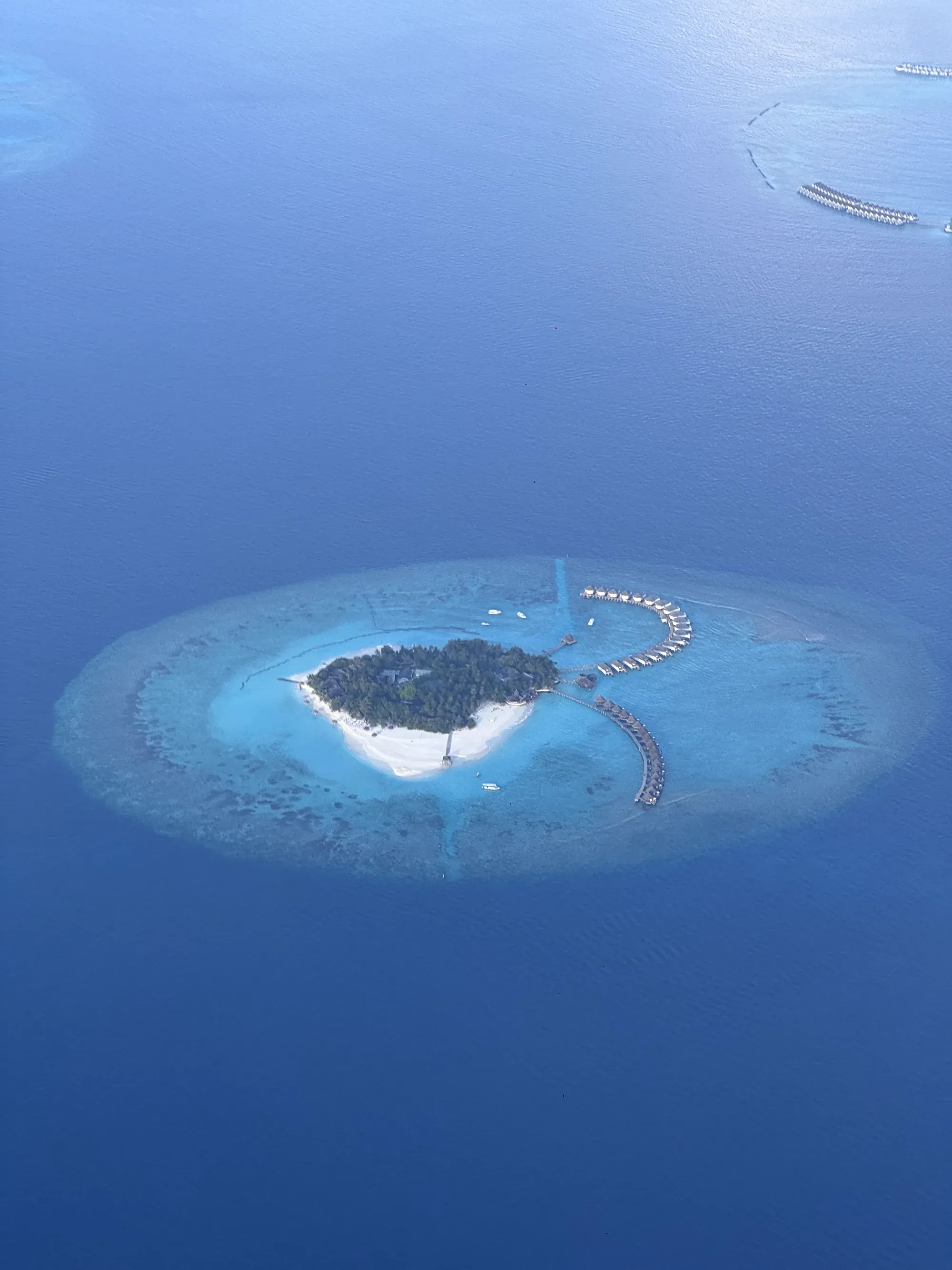 Aerial view of a Maldivian island resort with curved rows of water villas