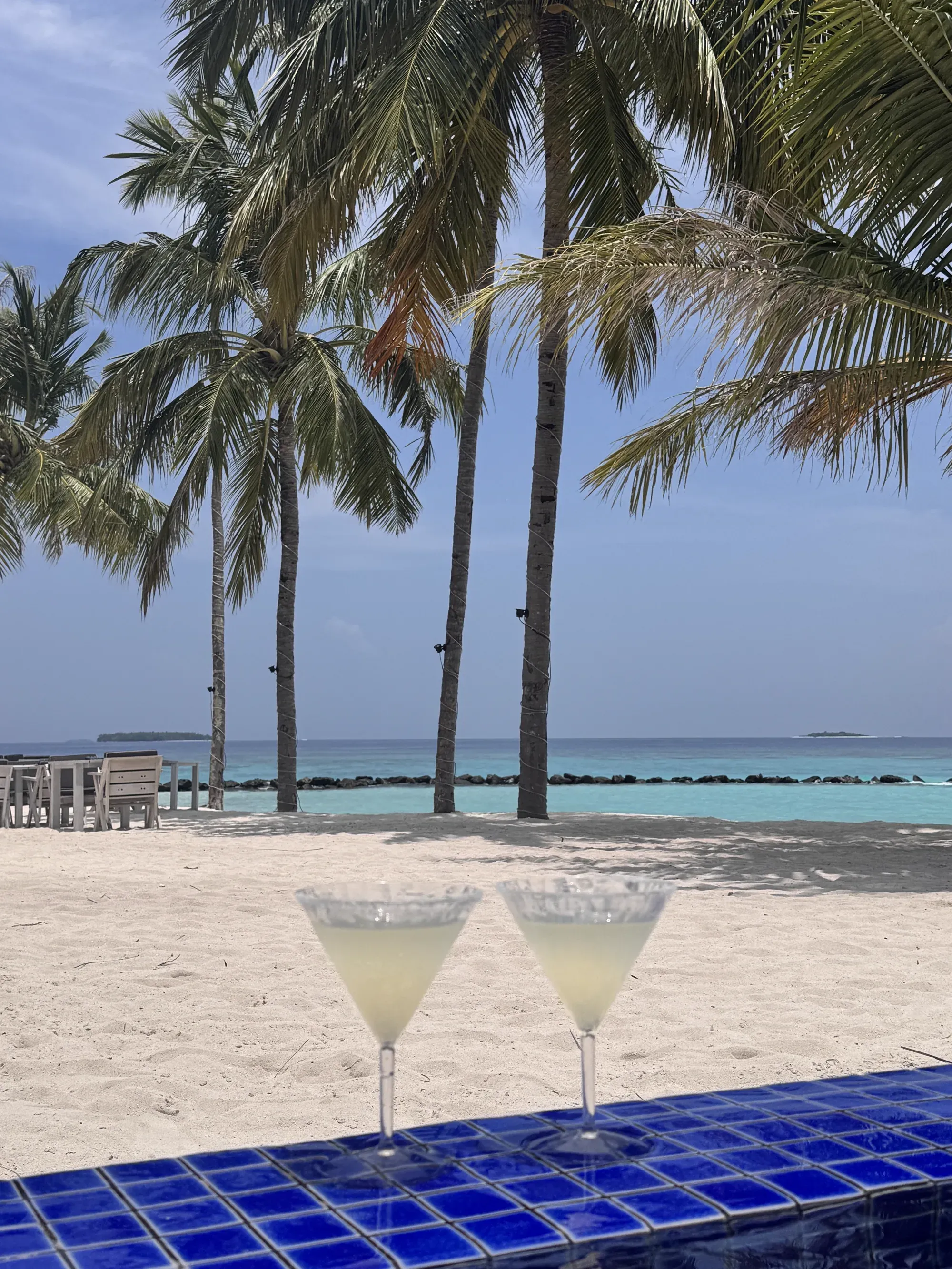 Two daiquiris on a blue tiled table looking out to palms and the lagoon at Emerald Maldives