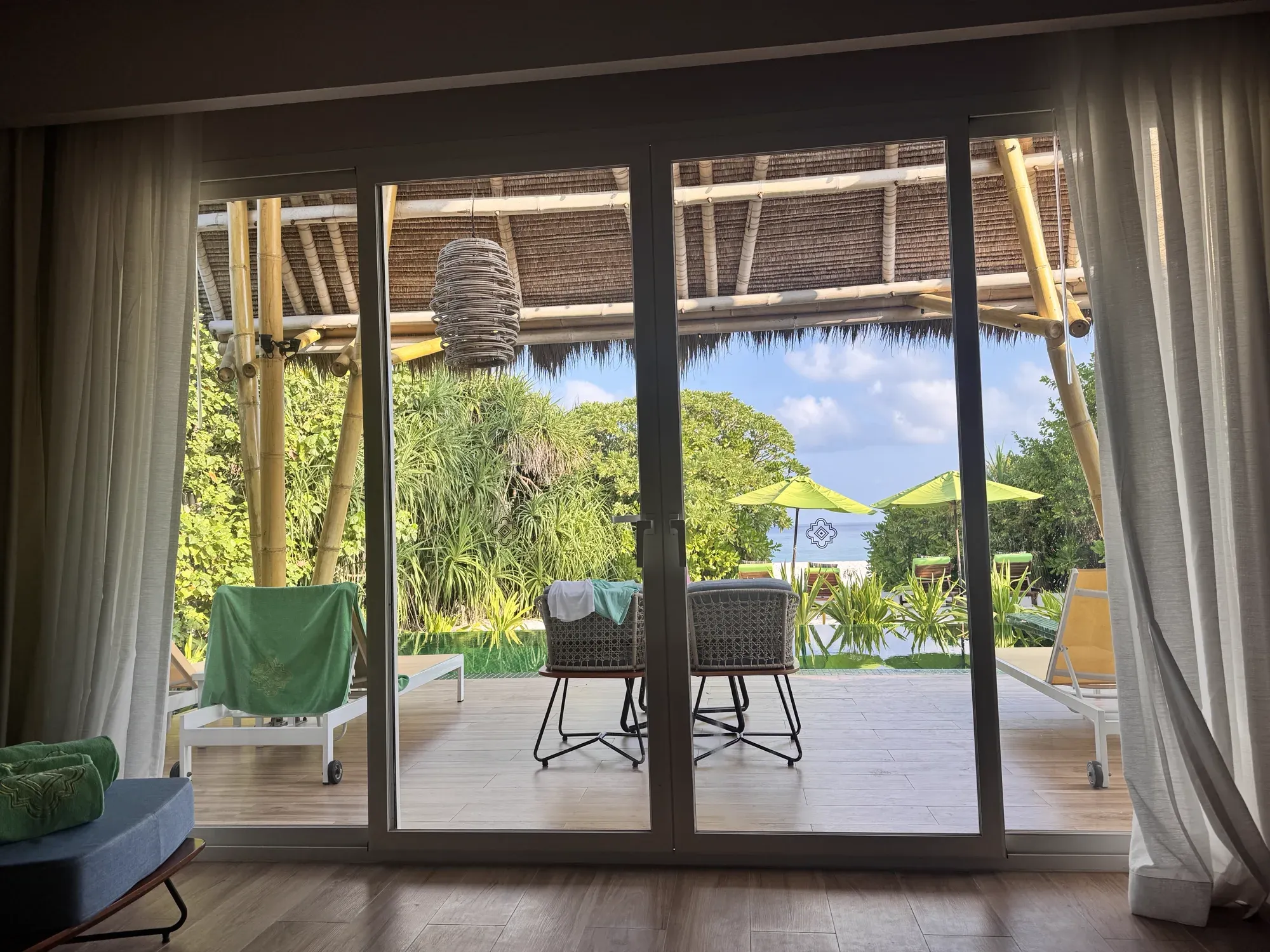View from inside a Beach Villa across the terrace to loungers and the sea at Emerald Maldives