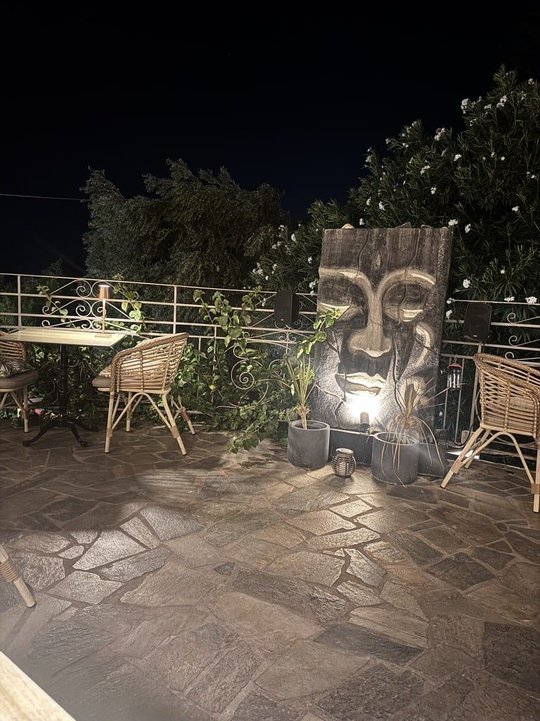 Stone face wall art on the terrace at night with rattan chairs at La Signora Hotel