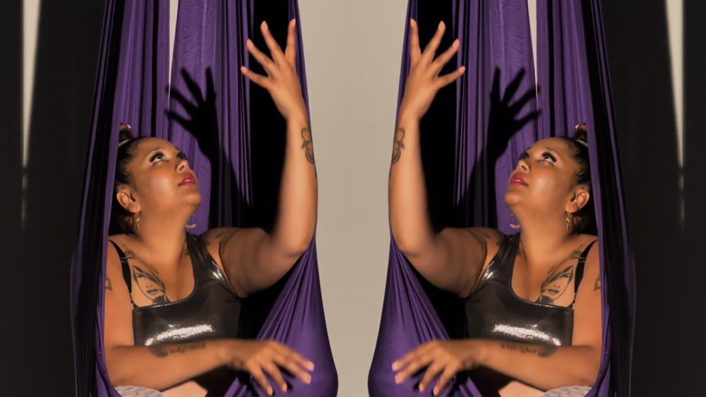 Gaitrie sits in a purple fabric used for aerial swings. The image is mirrored, so you see two Gaitries and two swings.
