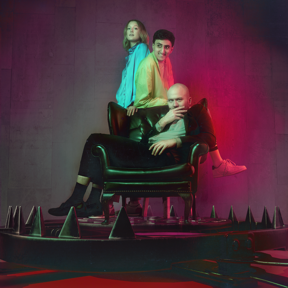 The three members from Flawbored are gathered around a large armchair.