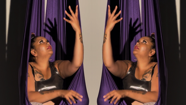 Gaitrie sits in a purple fabric used for aerial swings. The image is mirrored, so you see two Gaitries and two swings.