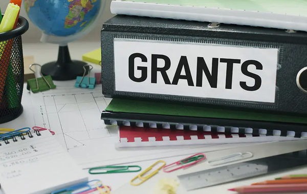 A binder labelled "GRANTS" sits on a desk, stacked on top of other folders.