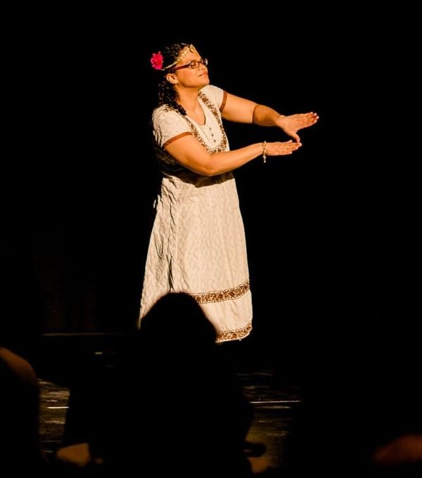 Tamyka Bullen spotlit on a dark stage wearing a traditional dress