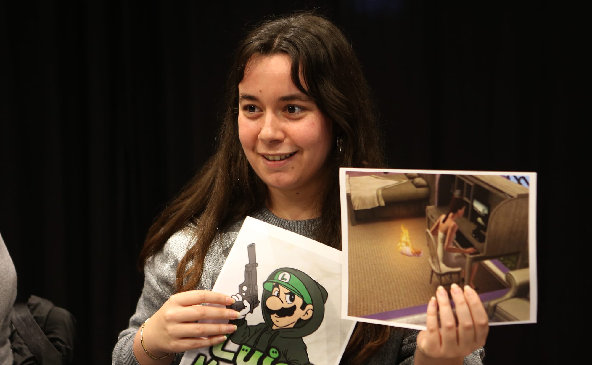 Foto de una de las personas asistentes sosteniendo dos memes, uno sobre Luigi Mangione y otro sobre los Sims