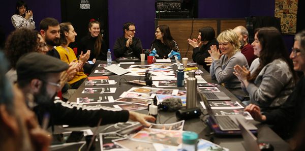 las personas asistentes al encuentro sentadas alrededor de una mesa. Se ven los memes de la dinàmica, ordenadores y caras sonrientes