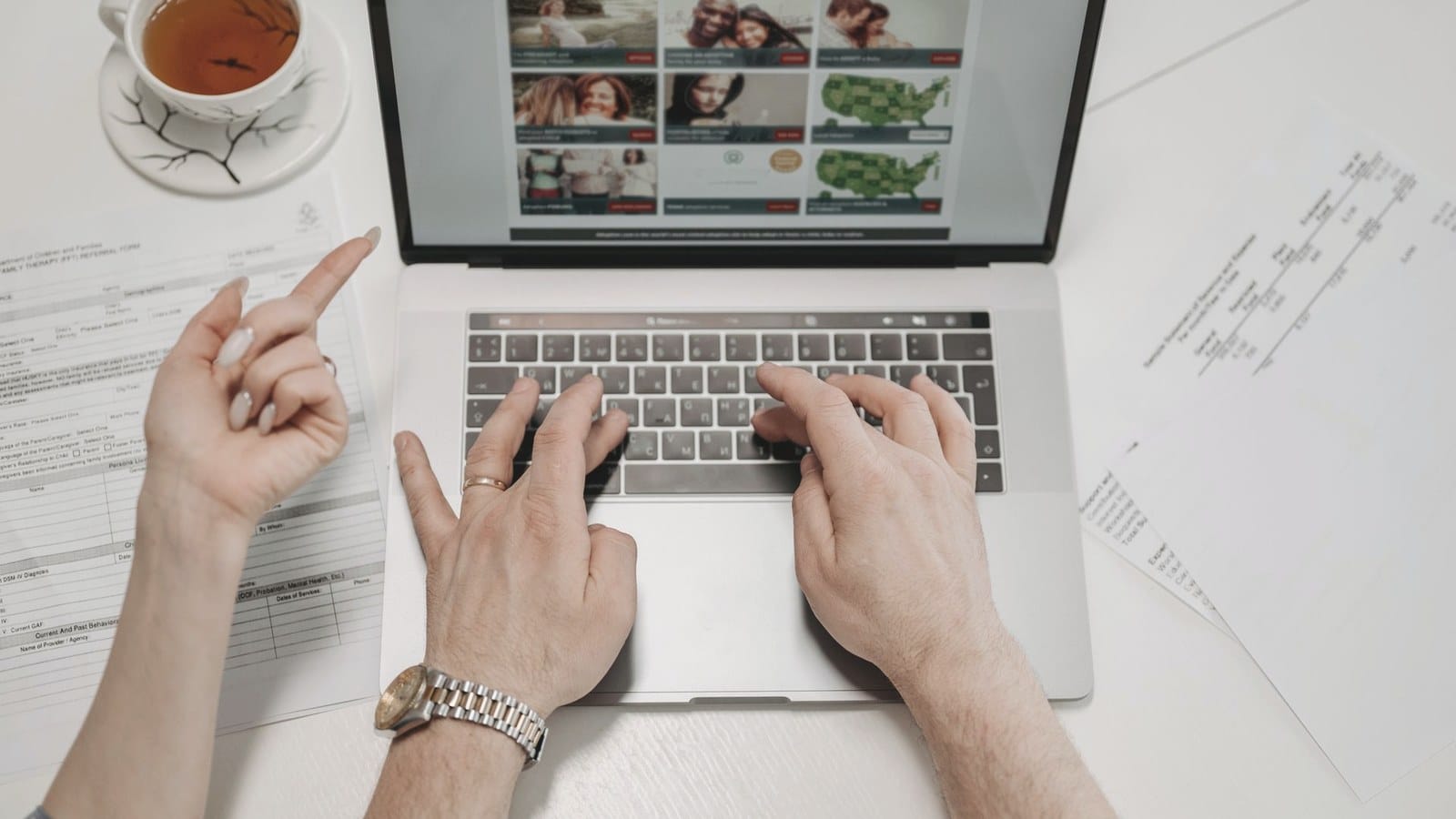 Hands type on a laptop next to paper documents on a desk.