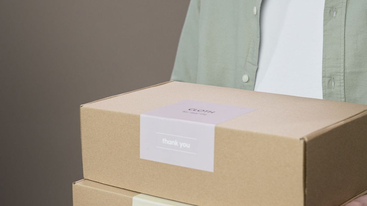 A person carries two cardboard boxes with visible labels on the front.
