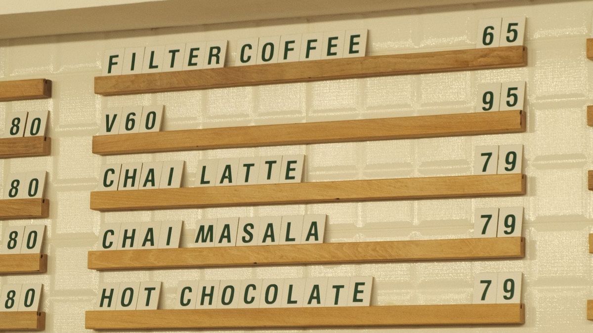 A cafe wall menu lists drink options and prices above a counter.