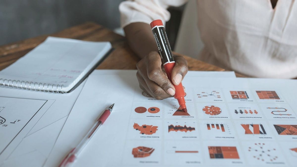 A person marks a paper document with a red marker.