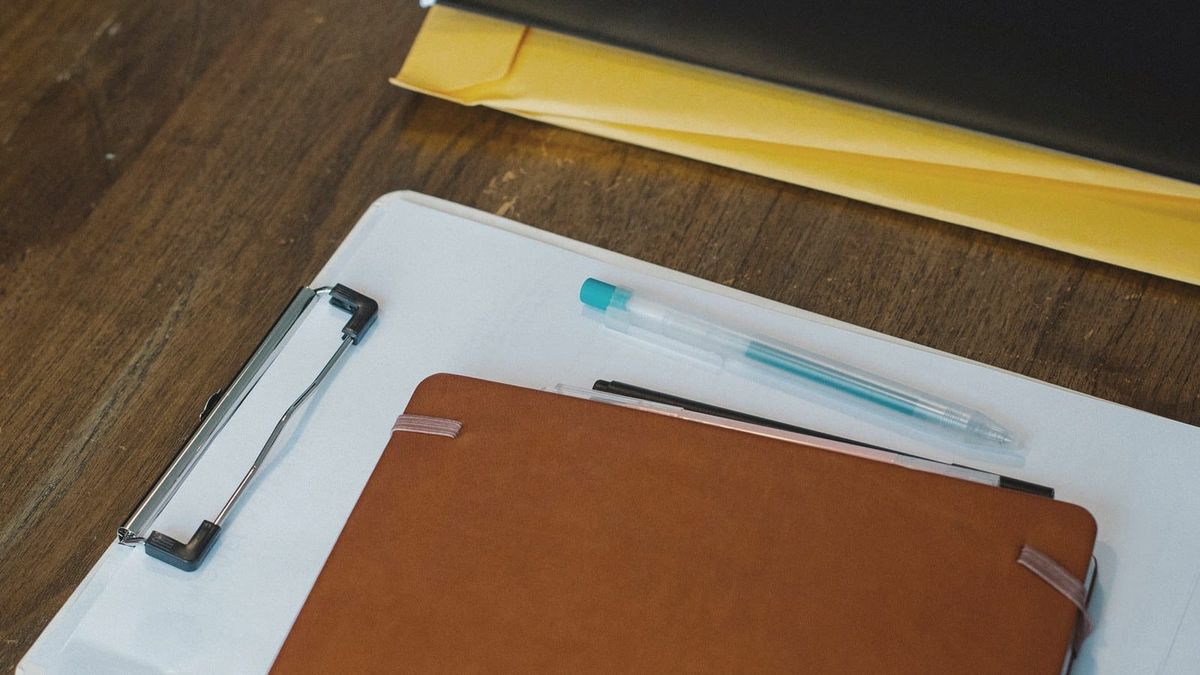A notebook, clipboard, folders, and pens arranged on a desk.