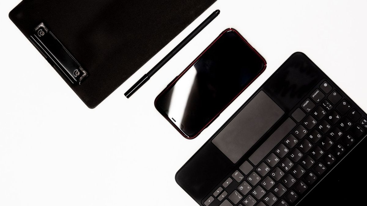 A smartphone, keyboard, pen, and clipboard arranged on a white work surface.
