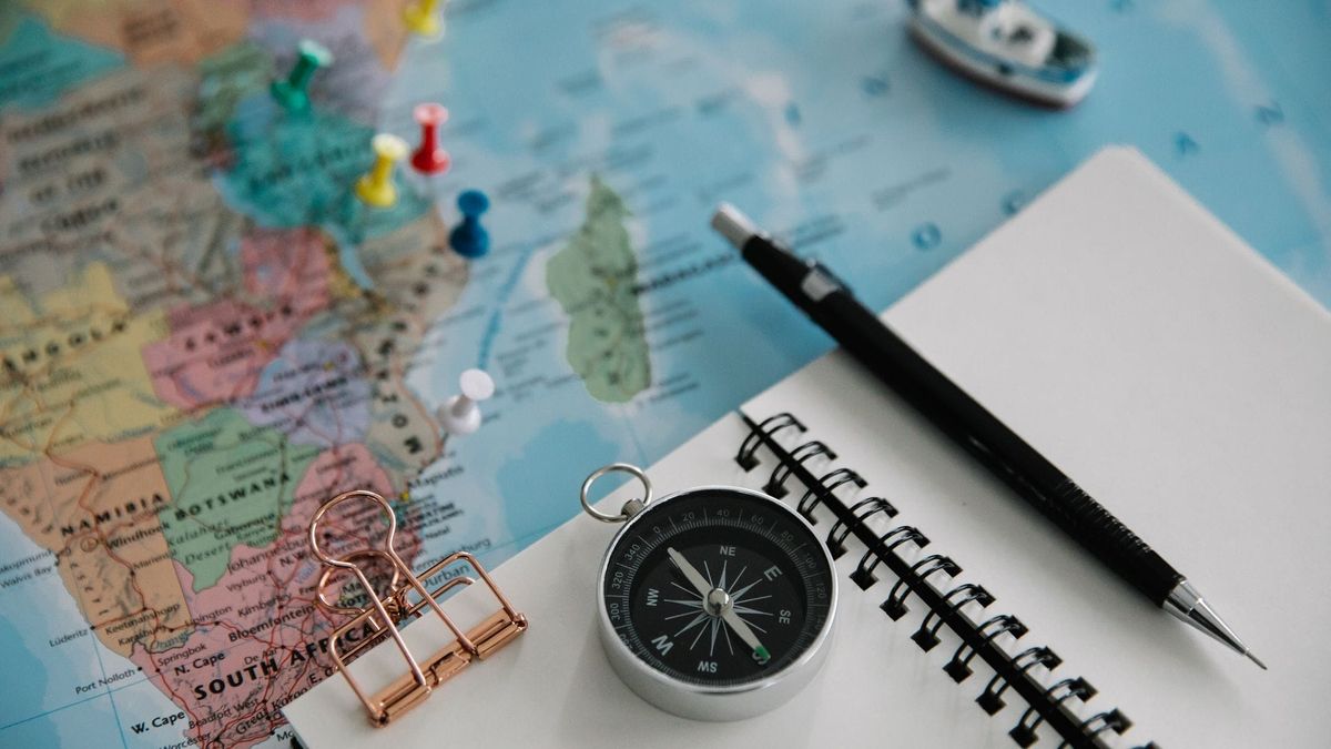 A notebook, pen, compass, and map arranged on a table.